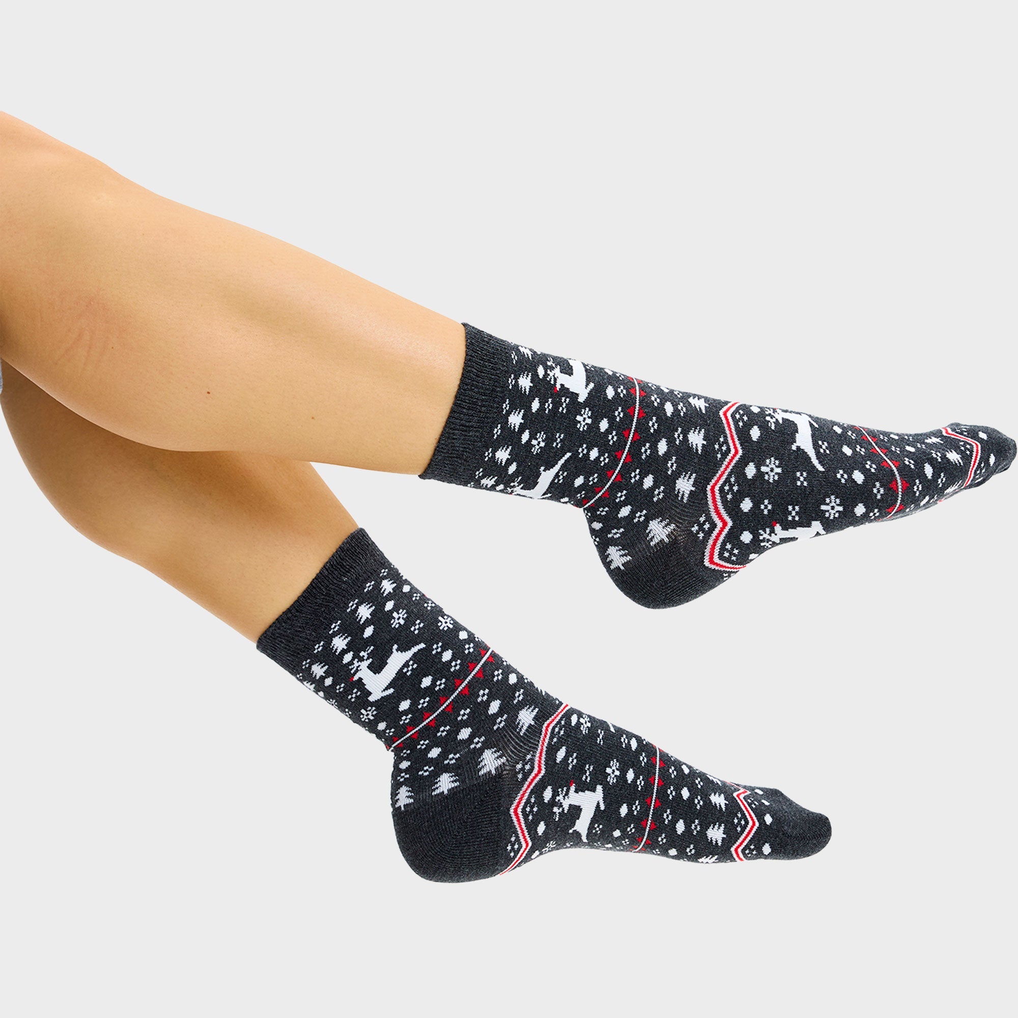 Ein Paar Füße, die schwarze Weihnachtssocken mit einem Muster darauf tragen.