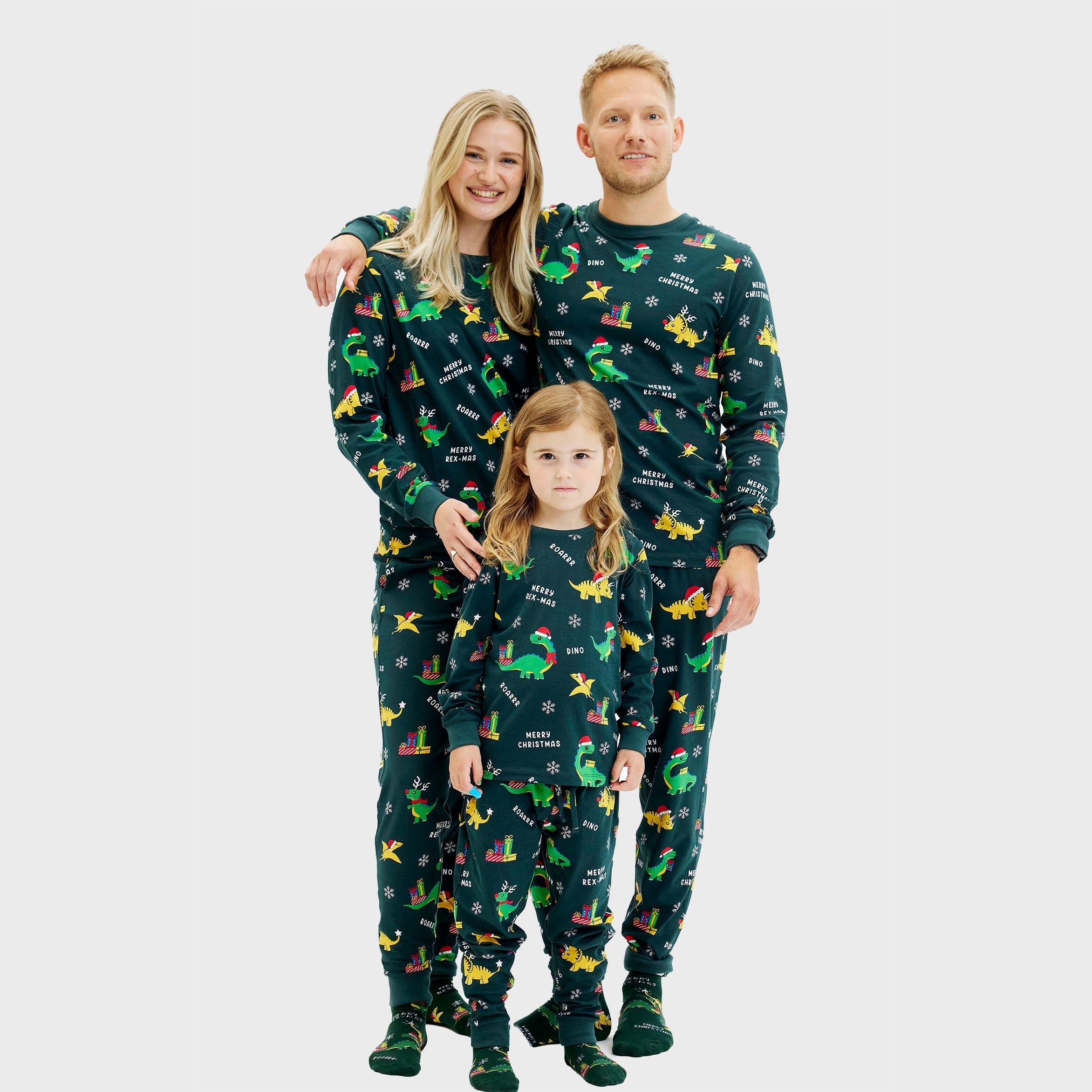 Drei-teiliger Dino Weihnachtspyjama für Damen, Herren und Kinder mit grünem Hintergrund und bunten Dinosauriermotiven.