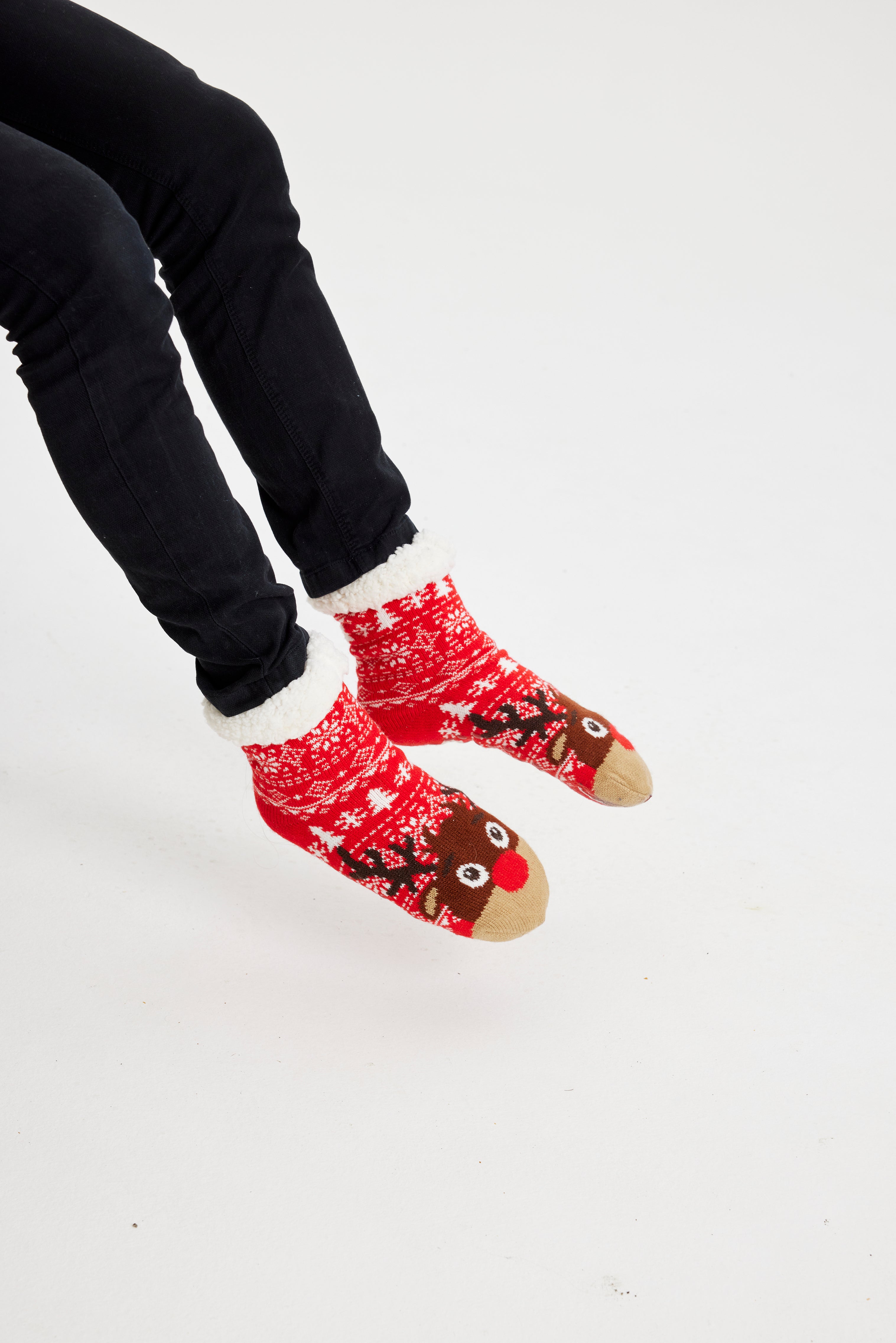 Ein Paar Beine, die ein Paar rote Weihnachtssocken mit einem Rentier darauf tragen.