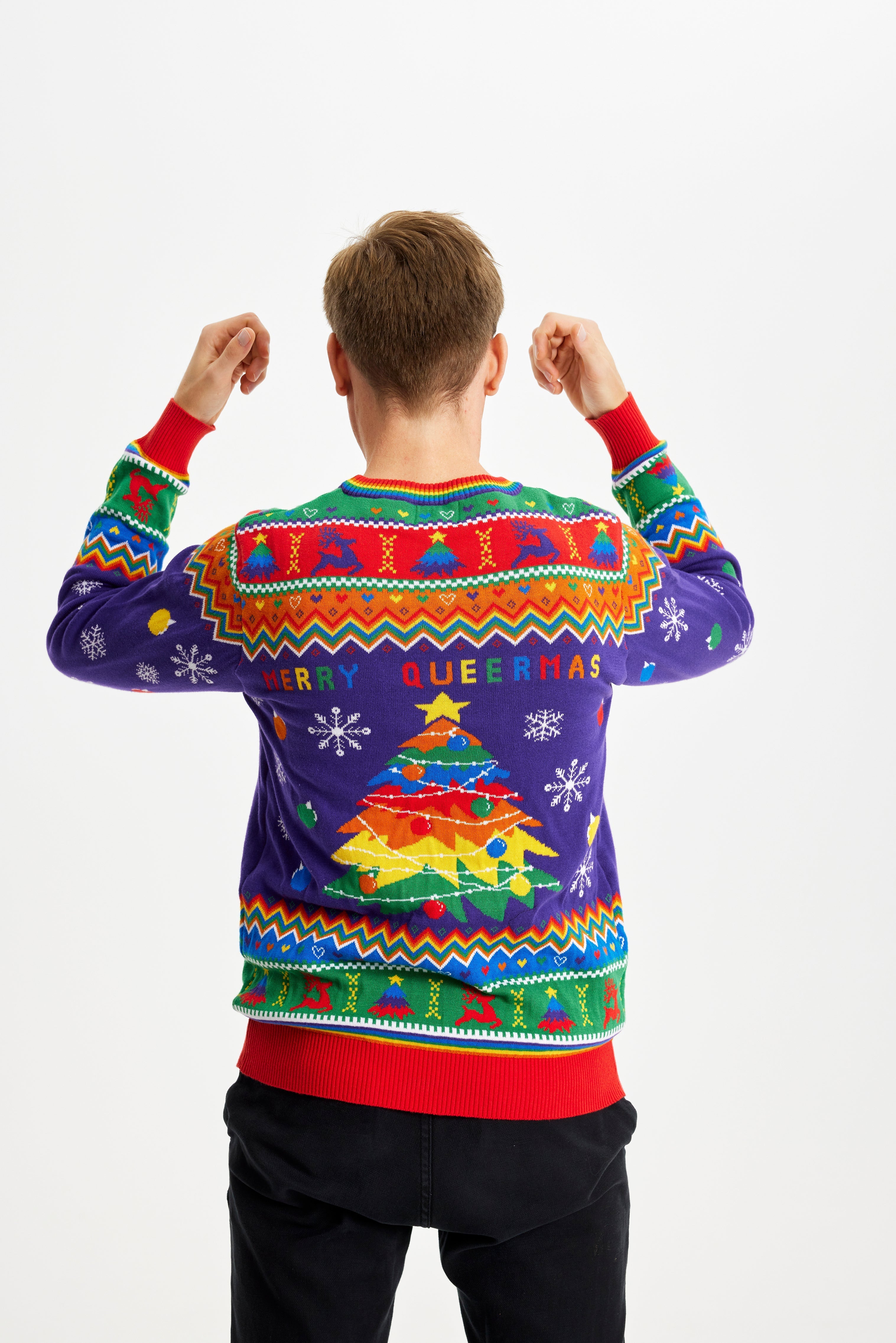 Ein posierender Mann mit dem Rücken zugewandt, der einen regenbogenfarbenen Weihnachtspulli mit dem Spruch 