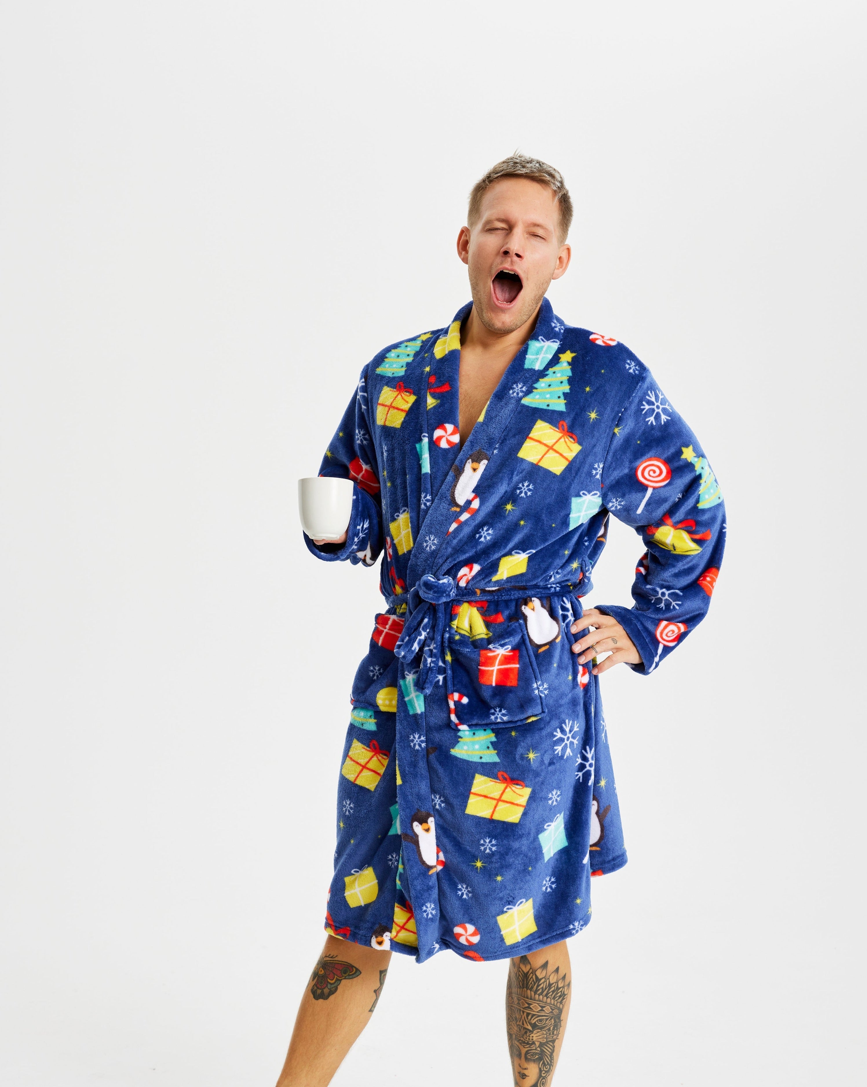 Ein gähnender Mann, der einen blauen Weihnachtsbademantel mit einem Weihnachtsmuster trägt.