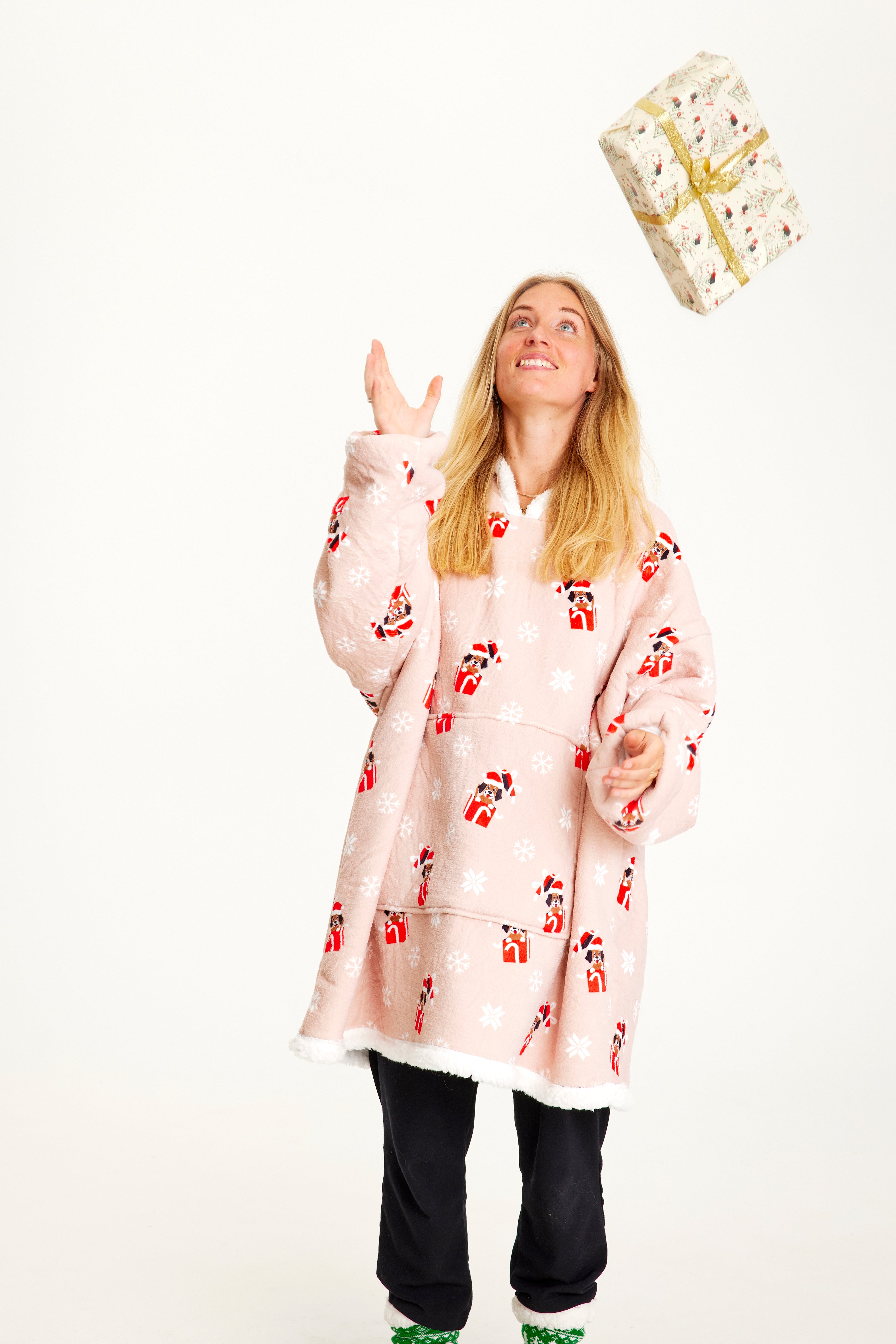 Eine Frau wirft ein Geschenk und trägt einen rosa Weihnachts-Kapuzenpullover mit Hunden darauf.